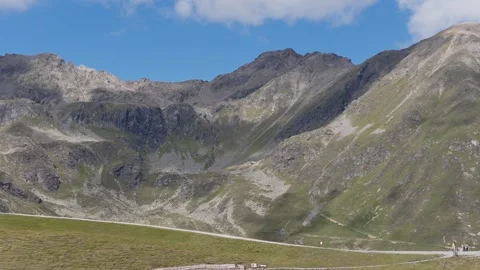 Distant Cyclist Rides a Scenic Mountain Road Winding Through Rugged Alpine Peaks Stock Footage 344288333