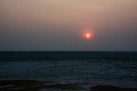 A distant dim sun sets in a clear sky over the evening desert Stock Photos