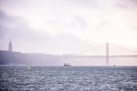 Distant ferry and 25 de Abril Bridge on Tagus River Stock Photos