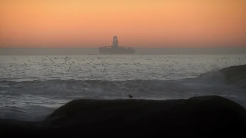 Distant floating drilling rig with orange sunset sky, grey sea Stock Footage 79888099