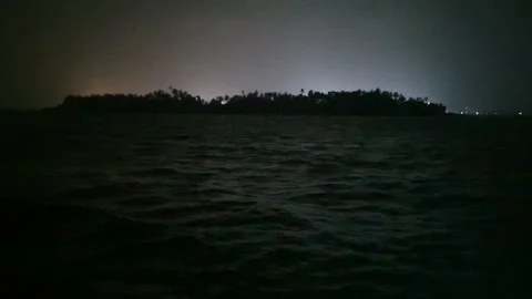Distant harbor lights illuminating behind a dark silhouette of a small island Stock Footage 346662487