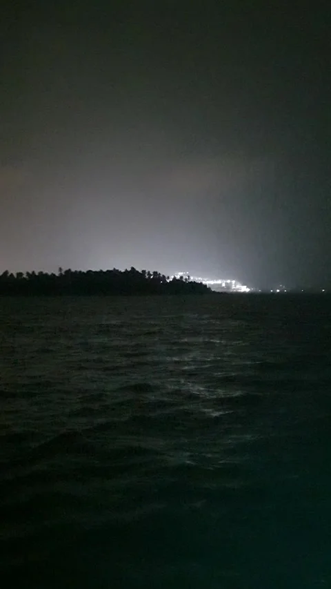 Distant harbor lights illuminating behind a dark silhouette of a small island Stock Footage 346662497