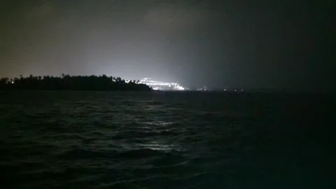 Distant harbor lights illuminating behind a dark silhouette of a small island Stock Footage 346662499