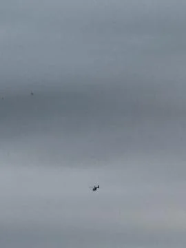 Distant Helicopter Flying Through Gray Overcast Sky 写真素材