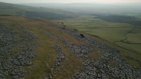 Distant hiker on rocky hillside with patchwork green fields and misty Stock-Footage 233882427