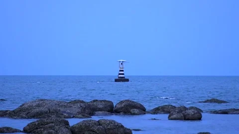 Distant lighthouse flashing red light at dusk with rocky beach coastline in the Stock Footage 314813082