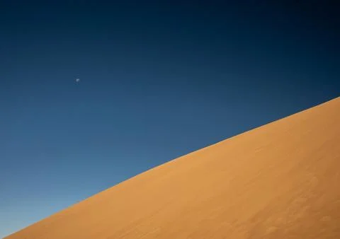 Distant Moon In Deep Blue Sky Against Bright Sand Dune Stock Photos