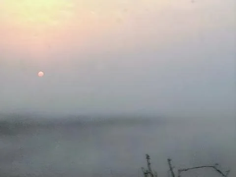 Distant pale orange sun barely visible through thick atmospheric moisture cr Stock Photos