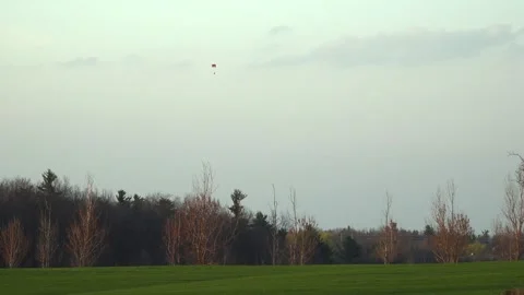 Distant Paraglider Flying Over Rural Farm Field at Sunset Stockbeeldmateriaal 345008092