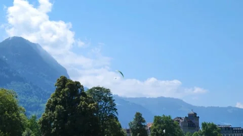 Distant paraglider soaring in blue sky above a historical Swiss castle. Anc.. Vidéo 348370052