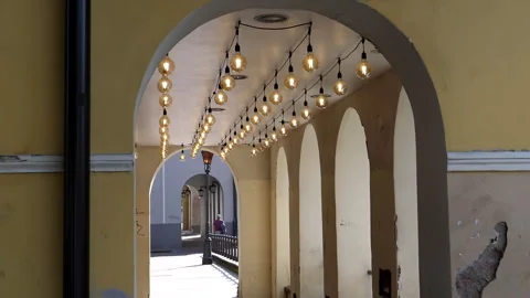 Distant people walking under arcade. Many lamps glowing on bright day Stock Footage 269395180