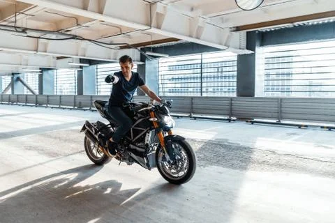 Distant plan of biker riding motorcycle at parking. Urban background. Stock Photos