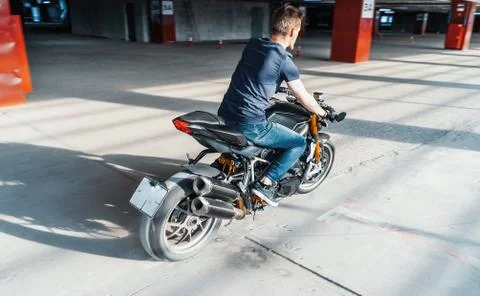 Distant plan of biker riding motorcycle at parking. Urban background. Stock Photos