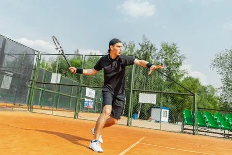 Distant plan of man playing tennis at court and beating the ball with a racket. Stock Photos