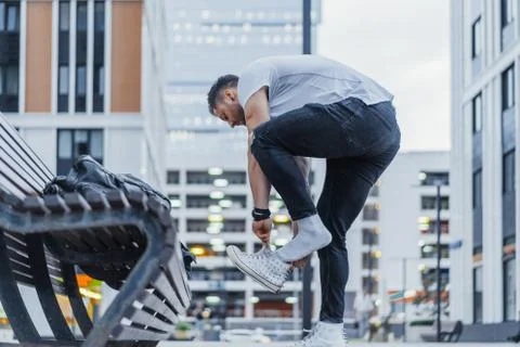 Distant plan of man putting on his white sneakers and standing next bench. Stock Photos