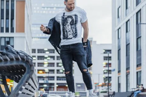 Distant plan of man putting on his black jacket and standing next to bench. Stock Photos