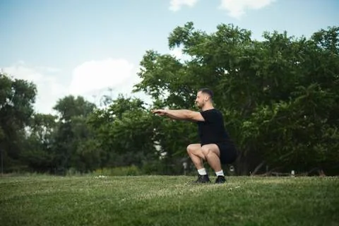 Distant plan of young attractive man squatting outdoor with outstretched hands. Foto stock