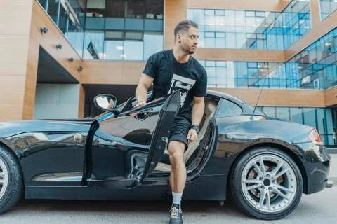 Distant plan of young attractive man getting out of the sport car. Side view. Stock Photos