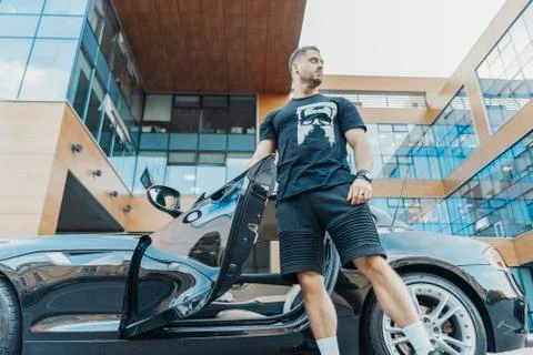 Distant plan of young attractive man getting out of the black sport car. Stock Photos