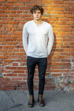 Distant plan of young attractive man standing on red brick background. Stock Photos