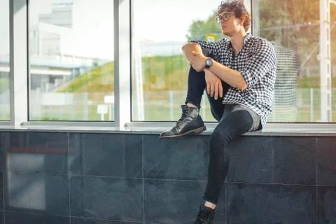 Distant plan of young man sitting next to big windows at metro station. Foto stock