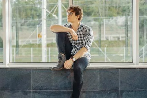 Distant plan of young man sitting next to big windows at metro station. Stock Photos