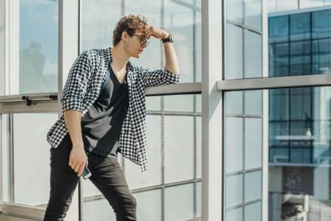 Distant plan of young man standing next to big windows at metro station. Stock Photos