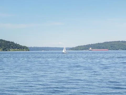 Distant sailboat and a cargo ship on Puget Sound under a bright sky in Ruston Fotos Stock