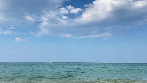 Distant sailboat glides across sea horizon beneath dramatic clouds and blue Stock Footage 337104824
