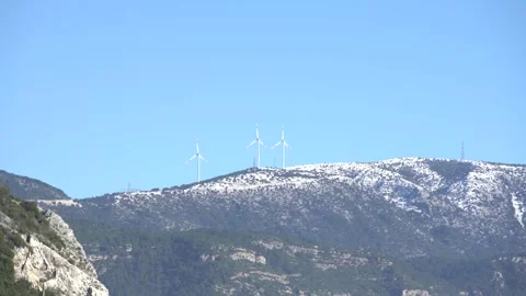 Distant shot, clear blue sky,3 wind turbines spinning over snow-capped mountains Stock Footage 142959866