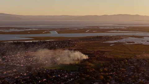 Distant Smoke Column Over Town and Tidal Wetlands in Hazy Golden Light 動画素材 341840237