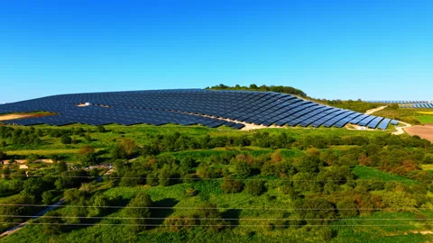 Distant solar array on a green hillside viewed across flowering fields. Dark Stock Footage 336386798