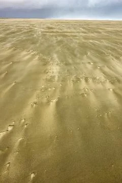 Distant storm clouds and windblown patterns with wind driven sand blowing a.. Stock Photos