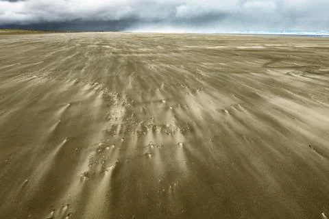 Distant storm clouds and windblown patterns with wind driven sand blowing a.. Stock Photos