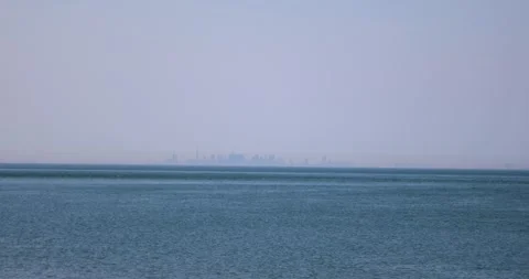 Distant Toronto skyline across calm blue lake haze with birds flying Stock Footage 320021674