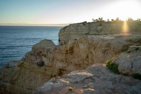 Distant view of couple standing on cliff by sea against clear sky at sunset Stock Photos