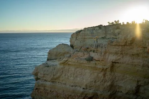 Distant view of couple walking on cliff by sea against clear sky at sunset Stock Photos