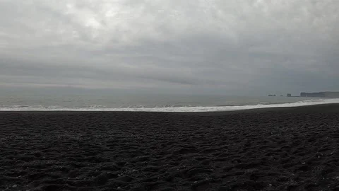 Distant view of Dyrholaey arch from Reynisfjara black sand beach, Iceland Stock Footage 334464164