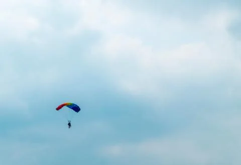 Distant view of man parachuting down against cloudy sky Foto stock