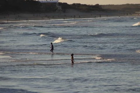 Distant view of people walking on beach and in water in the late afternoon Stock Photos