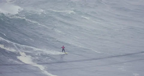 Distant view of pro surfer surfing down huge ocean wave during cloudy day Stock Footage 157716451