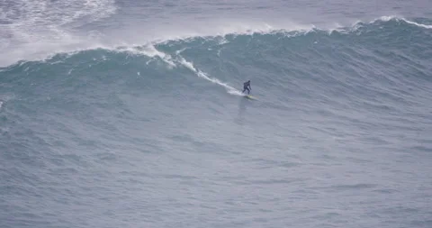 Distant view of professional surfer riding in ocean with big wave behind them Stock Footage 157723961