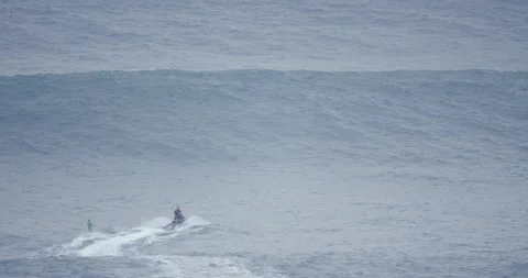 Distant view of professional surfer wake surfing behind jet ski driver in ocean Stock Footage 157708846