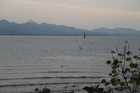 A distant view of the sea, with mountains in the background and an evening sk Stock Photos