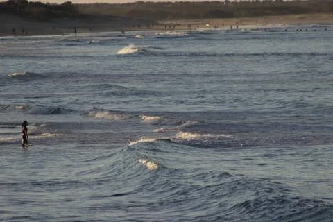 Distant view of waves and beach in the late afternoon with people Stock Photos