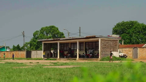 Distant wide shot of people under shelter with grass foreground, Betou, Congo Vídeos de archivo 338167514