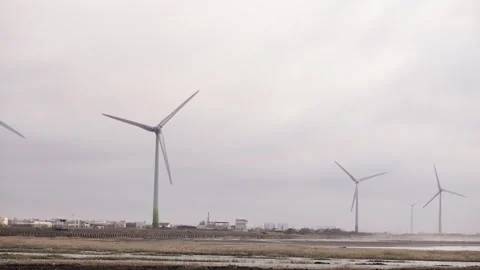 Distant wind turbines turning slowly on coast under overcast gray sky Stock Footage 312278027