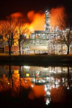 Distillation Tower of an oil refinery with reflection at night. The steam ill Stock Photos