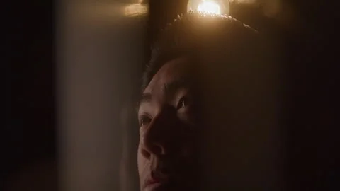 Distorted Close-up of Light Bulb Turning on Above Young Man in Dark Room Stock Footage 270305125