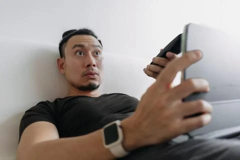 Distracted creative designer man lying on sofa working watching tv. Foto stock